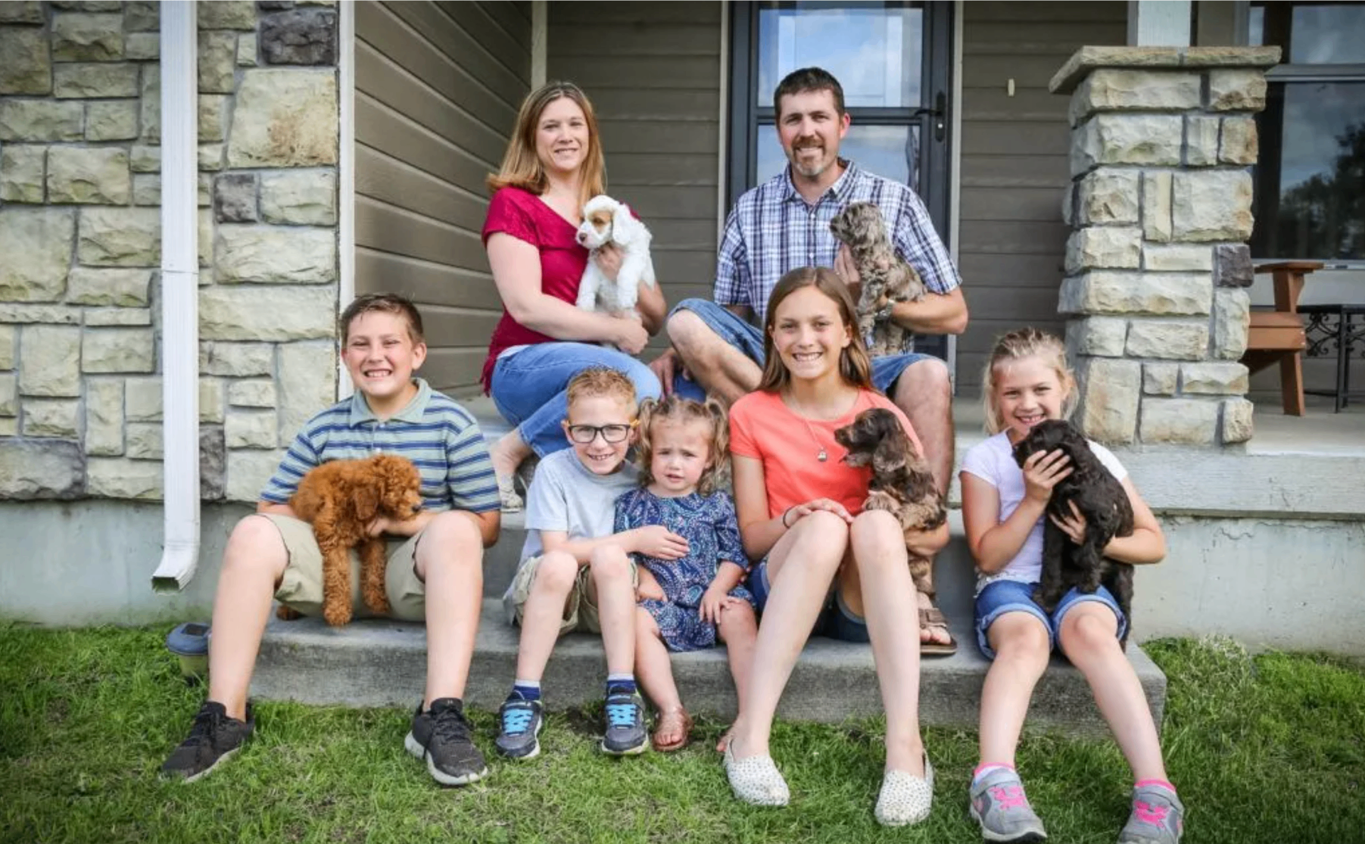 The Mueller family with their seven children and Australian Labradoodle puppies on the front porch